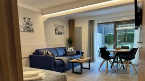 Een moderne woonkamer met een bank, een eettafel met stoelen, een bed met een gewatteerde spreideken en kunstwerken aan de muren.