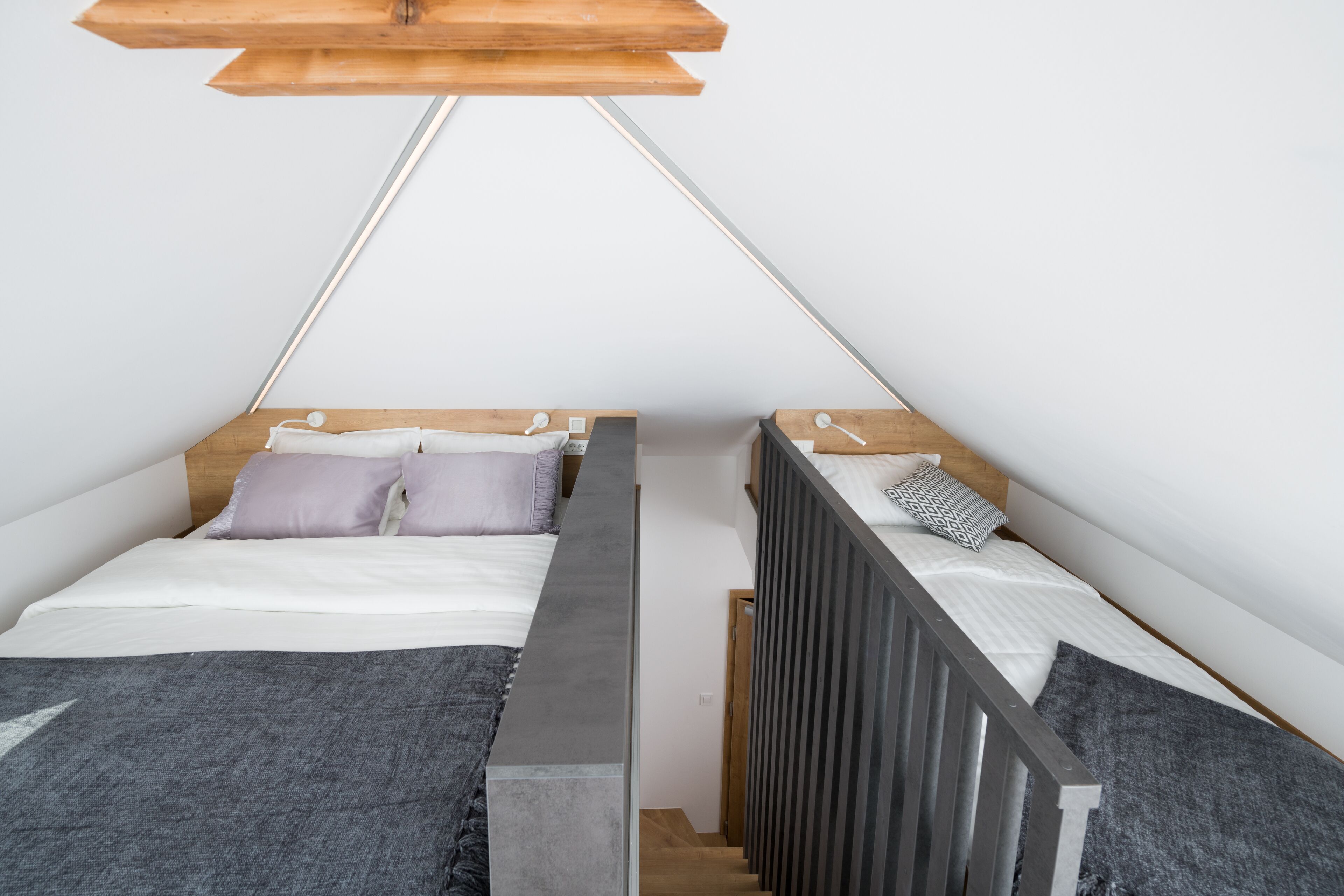 A small, modern bedroom with two beds, a concrete partition, and a wooden ceiling.