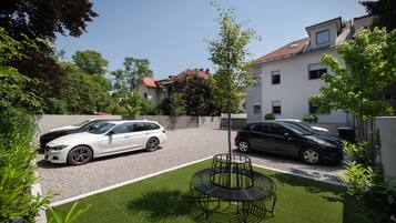 Een oprit met twee geparkeerde auto's, een verzorgd gazon en een metalen tuin stoel.