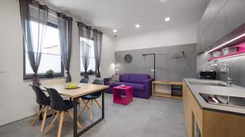 Una cucina moderna con zona pranzo, un divano viola e un piccolo tavolo con un comodino rosa.