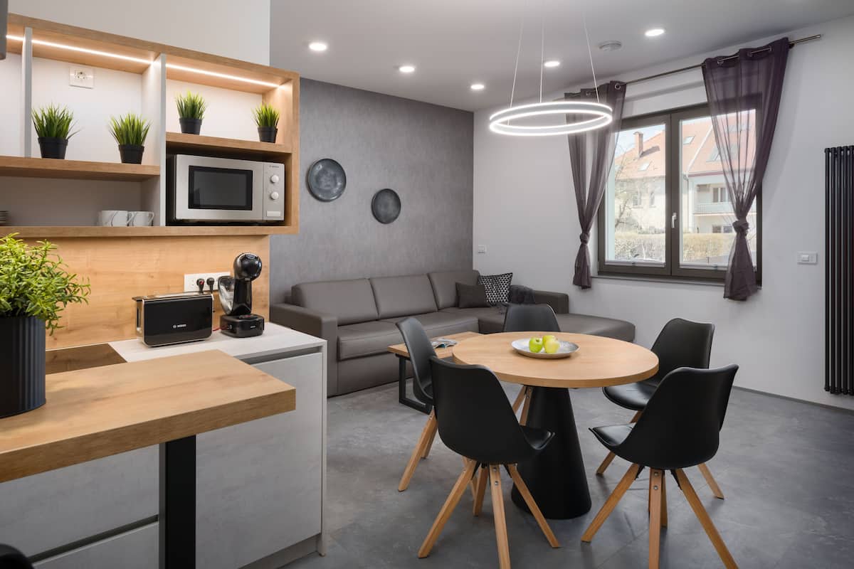 Een moderne keuken met een magnetron, broodrooster en koffiezetapparaat op het aanrecht. Er is een eethoek met een ronde tafel en zwarte stoelen.