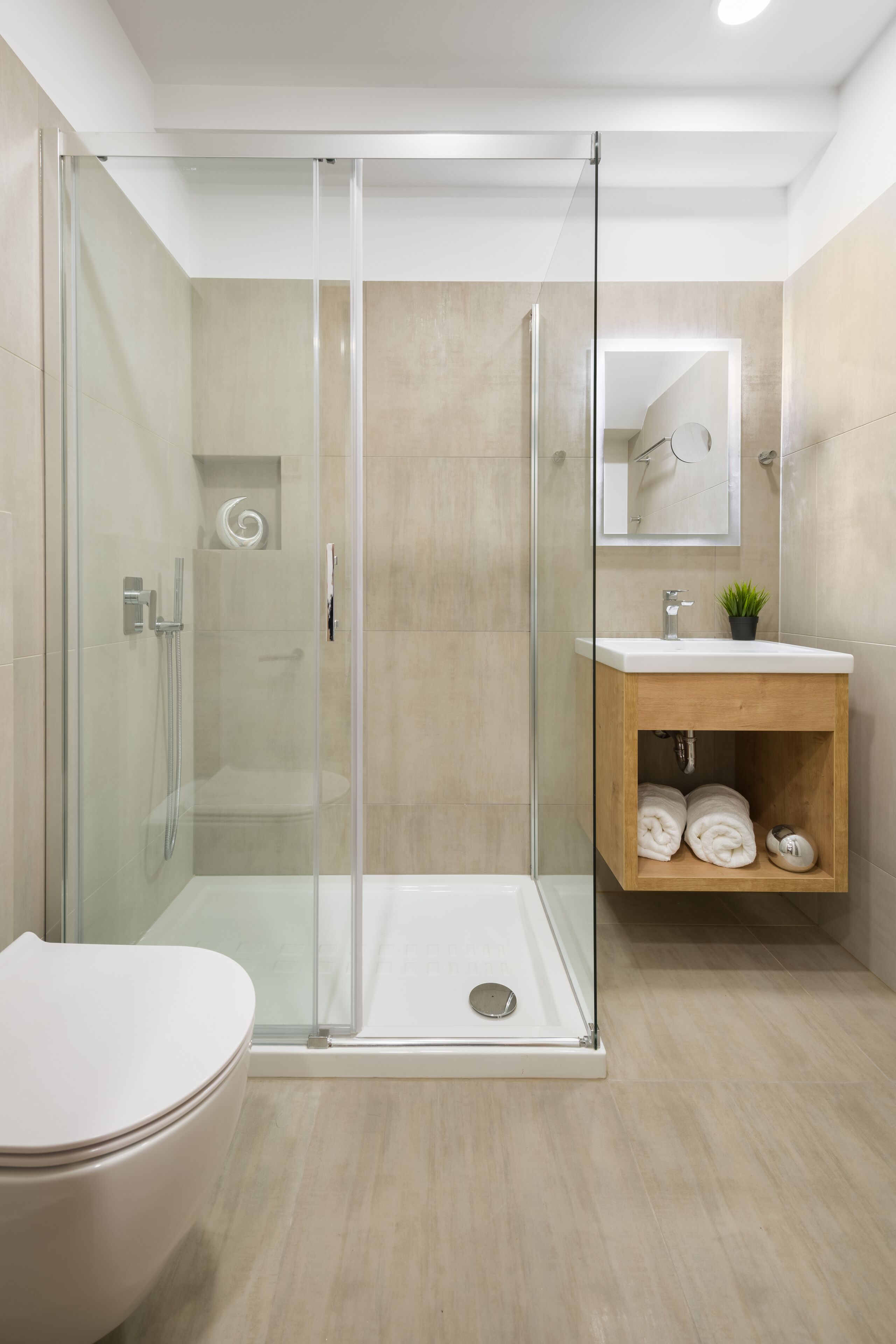 A modern bathroom with a glass-enclosed shower, a white toilet, and a wooden vanity with a mirror.