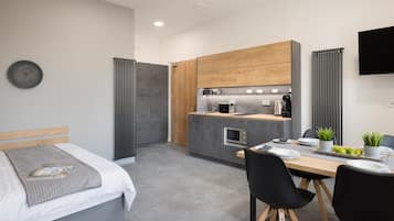 A modern hotel room with a bed, bedside table, and a small kitchenette.