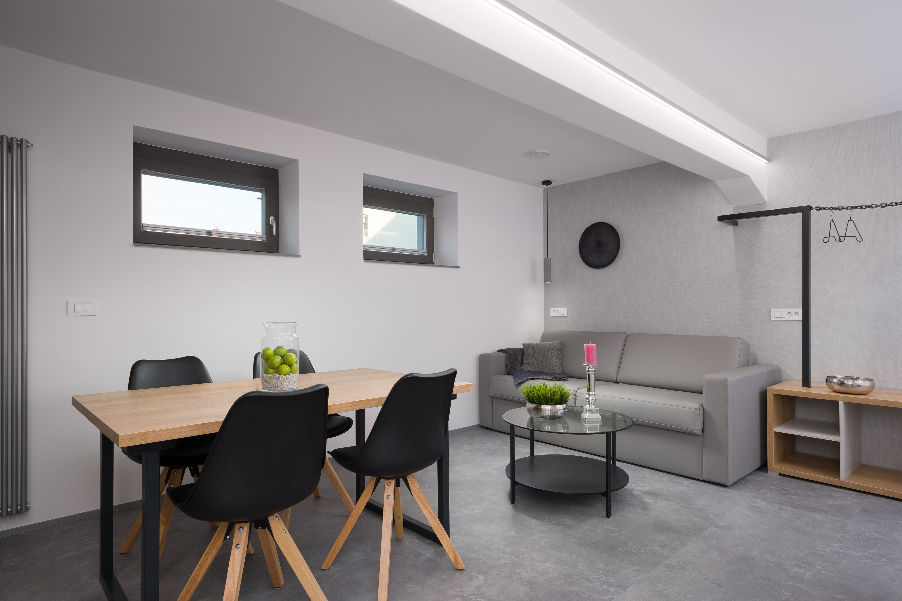 A modern living room with a wooden dining table, black chairs, a grey sofa, and a glass coffee table.