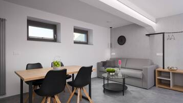 A modern living room with a wooden dining table, black chairs, a grey sofa, and a glass coffee table.