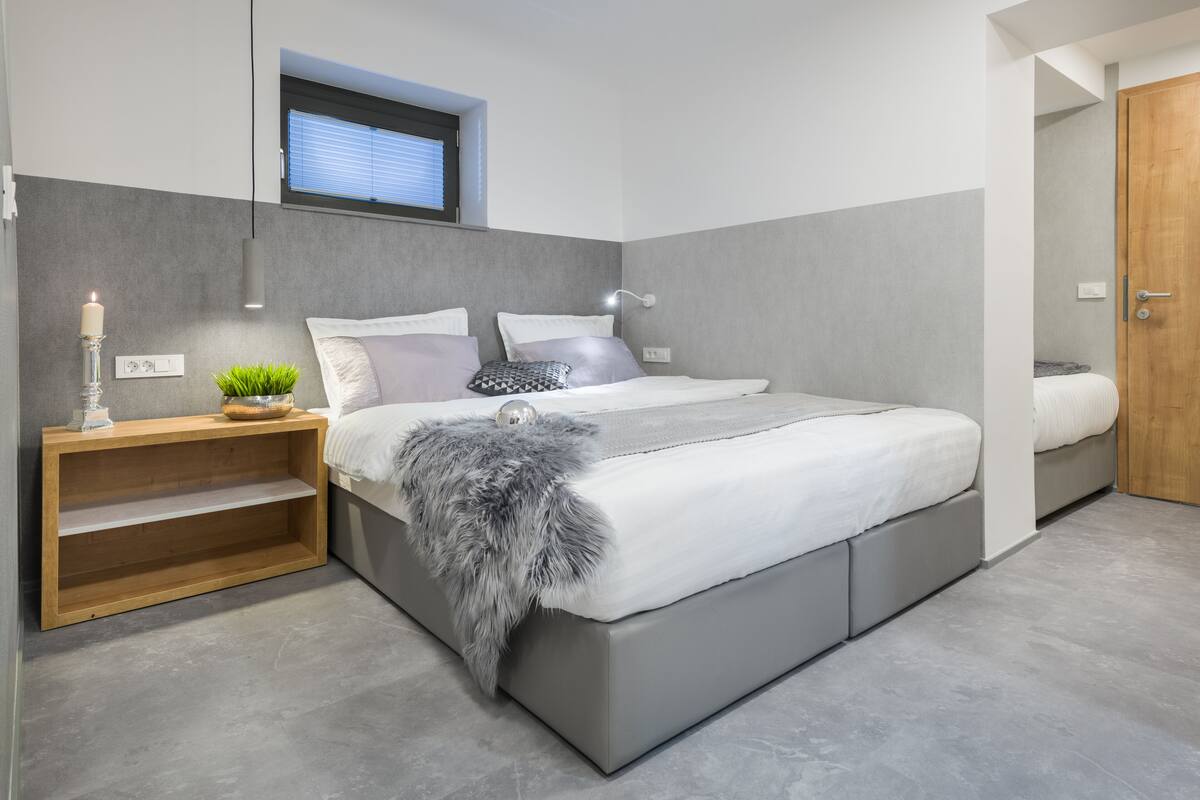Een moderne slaapkamer met een groot bed, een nachtkastje met een plant, een tv aan de muur en een houten deur.