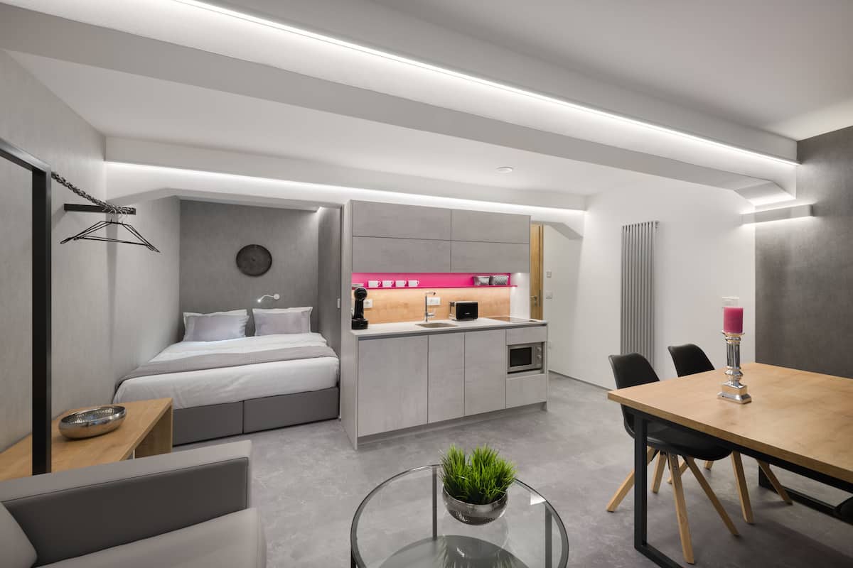Een moderne hotelkamer met een bed, een kleine kitchenette, een zithoek en een glazen tafel met een plant.