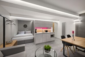 Een moderne hotelkamer met een bed, een kleine kitchenette, een zithoek en een glazen tafel met een plant.