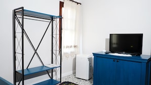 Una habitación con un armario azul, un refrigerador blanco, una estantería azul y un televisor encima del armario.