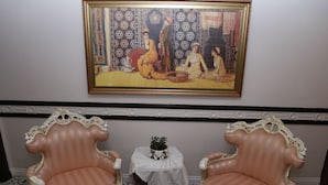Una habitación con dos sillas ornamentadas, una mesita con una planta y un cuadro grande en la pared.