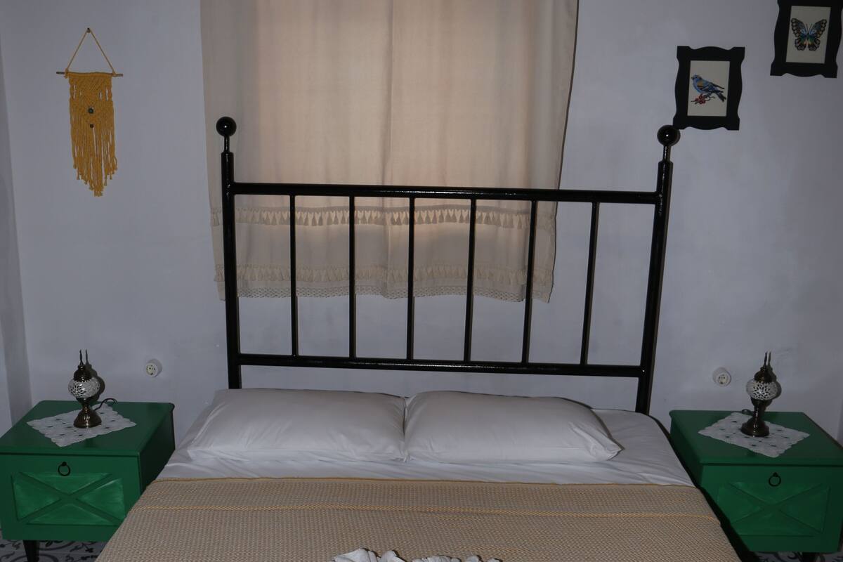 A neatly made bed with white linens, two green nightstands with lamps, and a simple wall decor.
