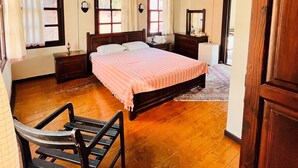 Un dormitorio espacioso con una cama grande, pisos de madera, ventilador de techo y varias ventanas.