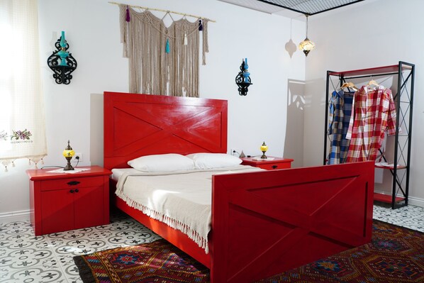 A red bed with white pillows, a red nightstand, a red wardrobe, and a clothing rack with plaid shirts.