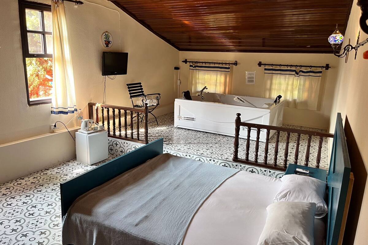 A bedroom with a bed, a white sofa, a small table, a TV, and a window with curtains.