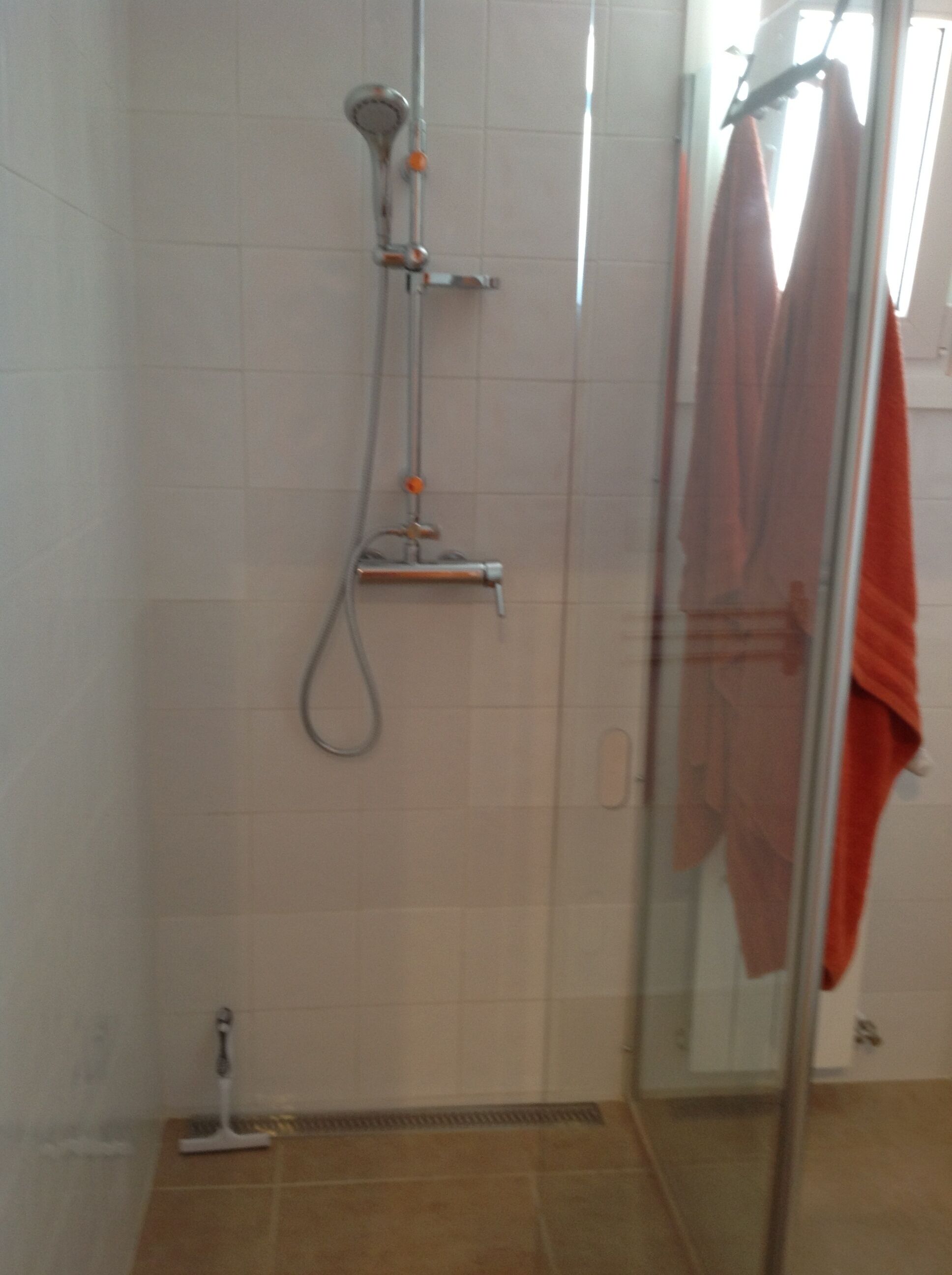 Een douche met een glazen deur, een handdoekhouder met een handdoek en een douchekop.