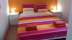 Cama com roupa de cama listrada e duas almofadas, duas luminárias de cabeceira e duas toalhas dobradas sobre a cama.