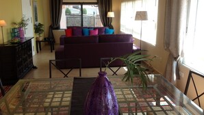 Uma sala de estar com sofá, mesa de jantar e um vaso roxo.