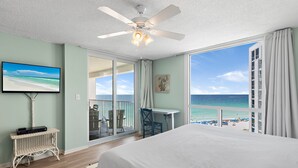 Quarto com cama grande, ventoinha no teto, televisão, arranhador para gatos e varanda com vista para a praia.