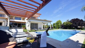 Area piscina con poltrone relax, una bottiglia di champagne e un bicchiere di vino.