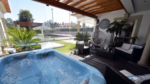 Una vasca idromassaggio in una zona esterna coperta con vista su una piscina e del verde.