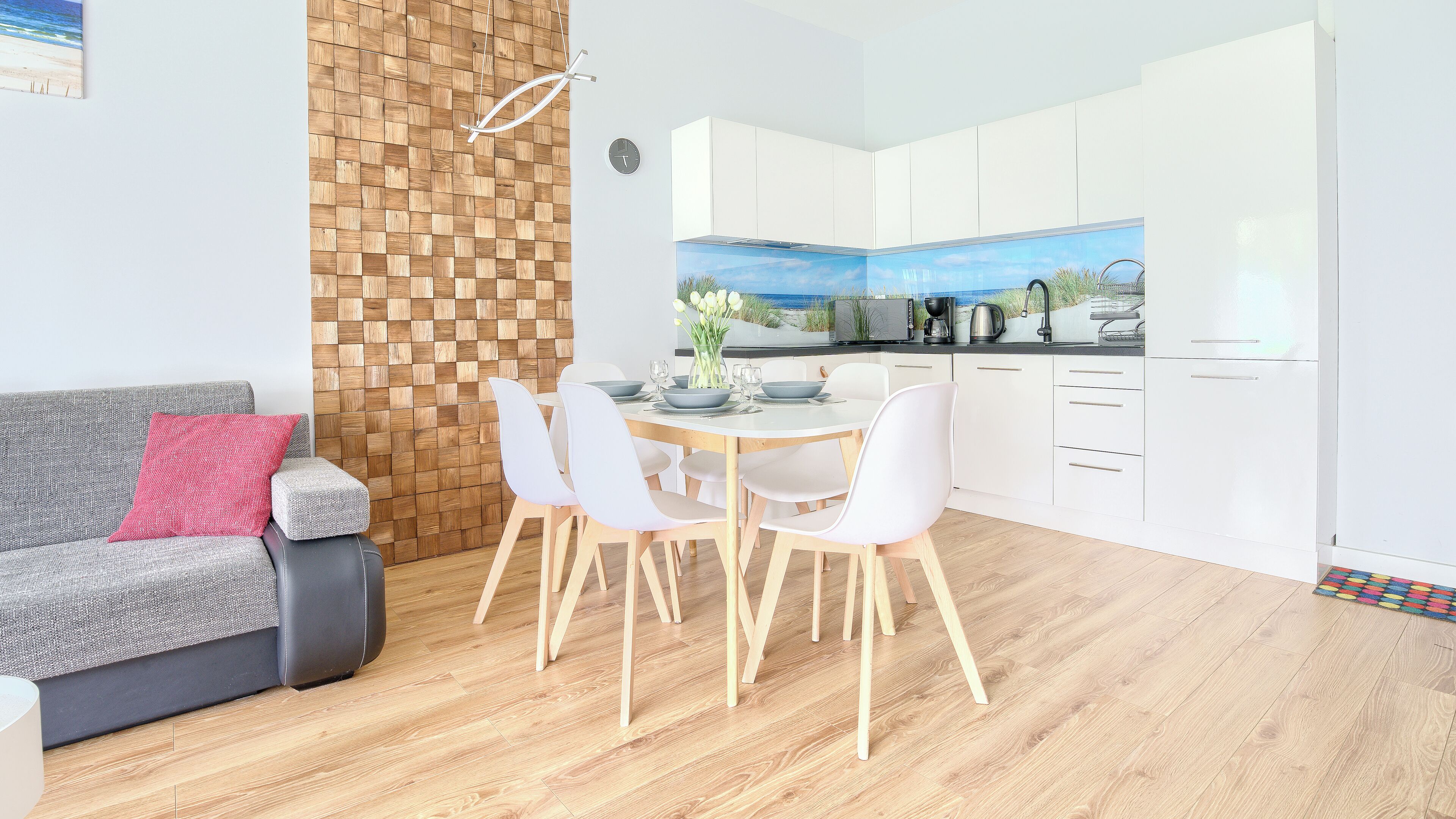 A modern kitchen with white cabinets, a dining table with white chairs, and a wooden floor.