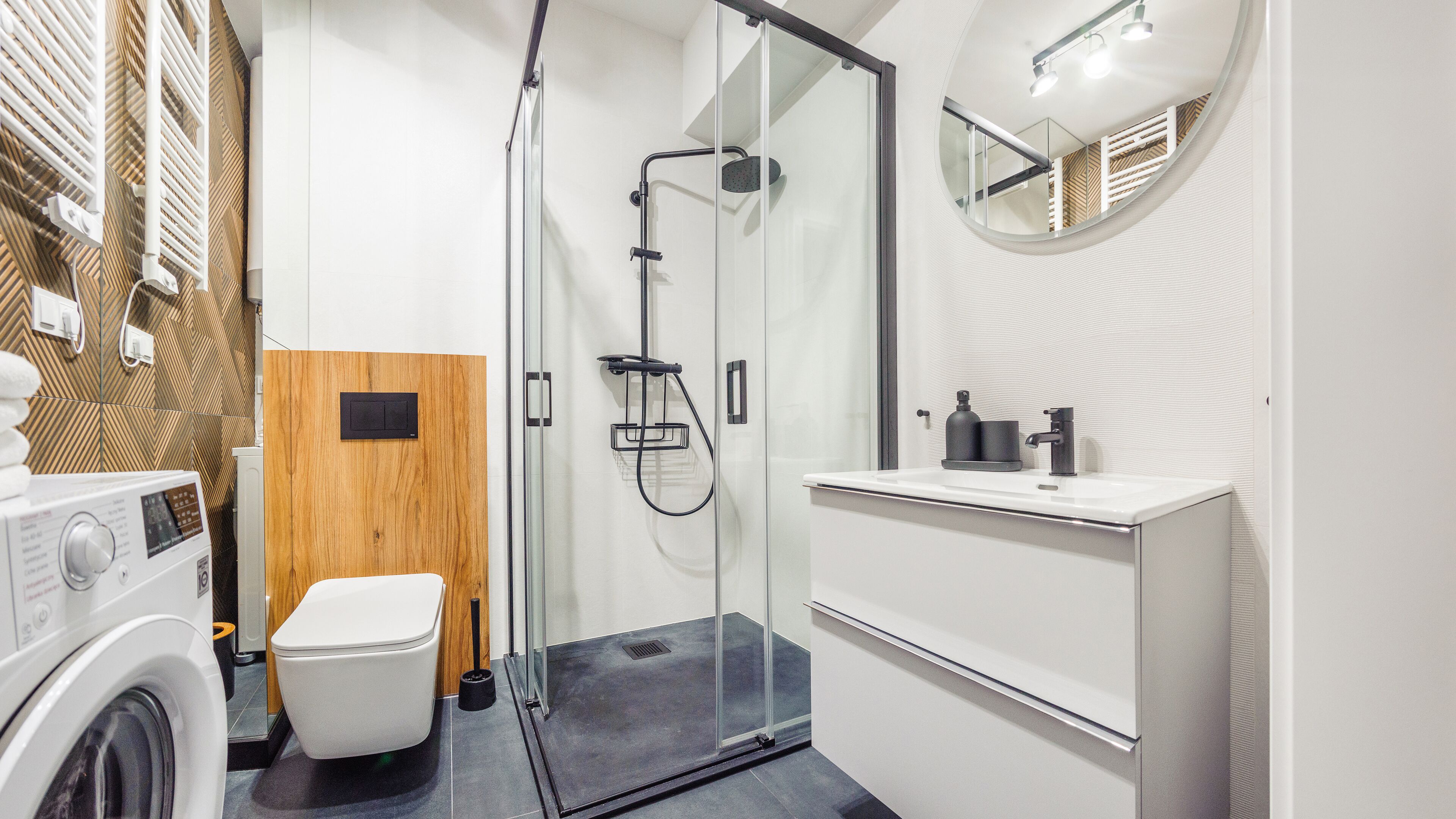 Un bagno moderno con cabina doccia in vetro, un water bianco, una lavatrice e un lavandino con specchio.