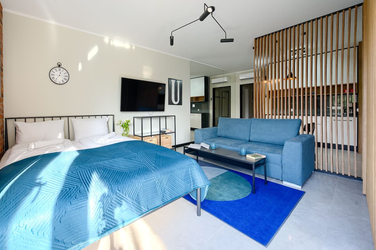Een moderne slaapkamer met een bed, een blauwe bank, een salontafel en een aan de muur bevestigde televisie.