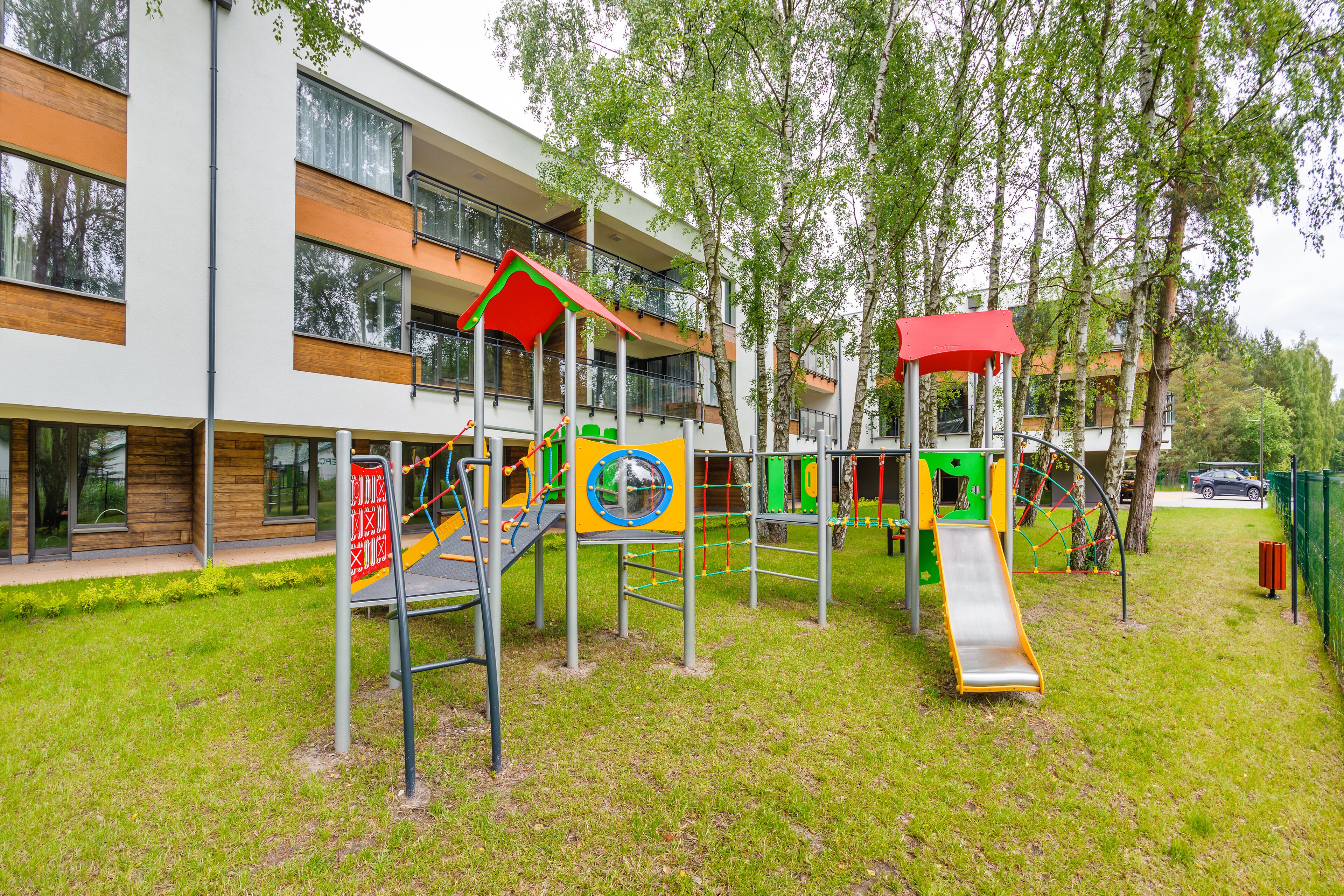 Ein Spielplatz mit Rutschen und Klettergerüsten, umgeben von einer Wiese und Bäumen.