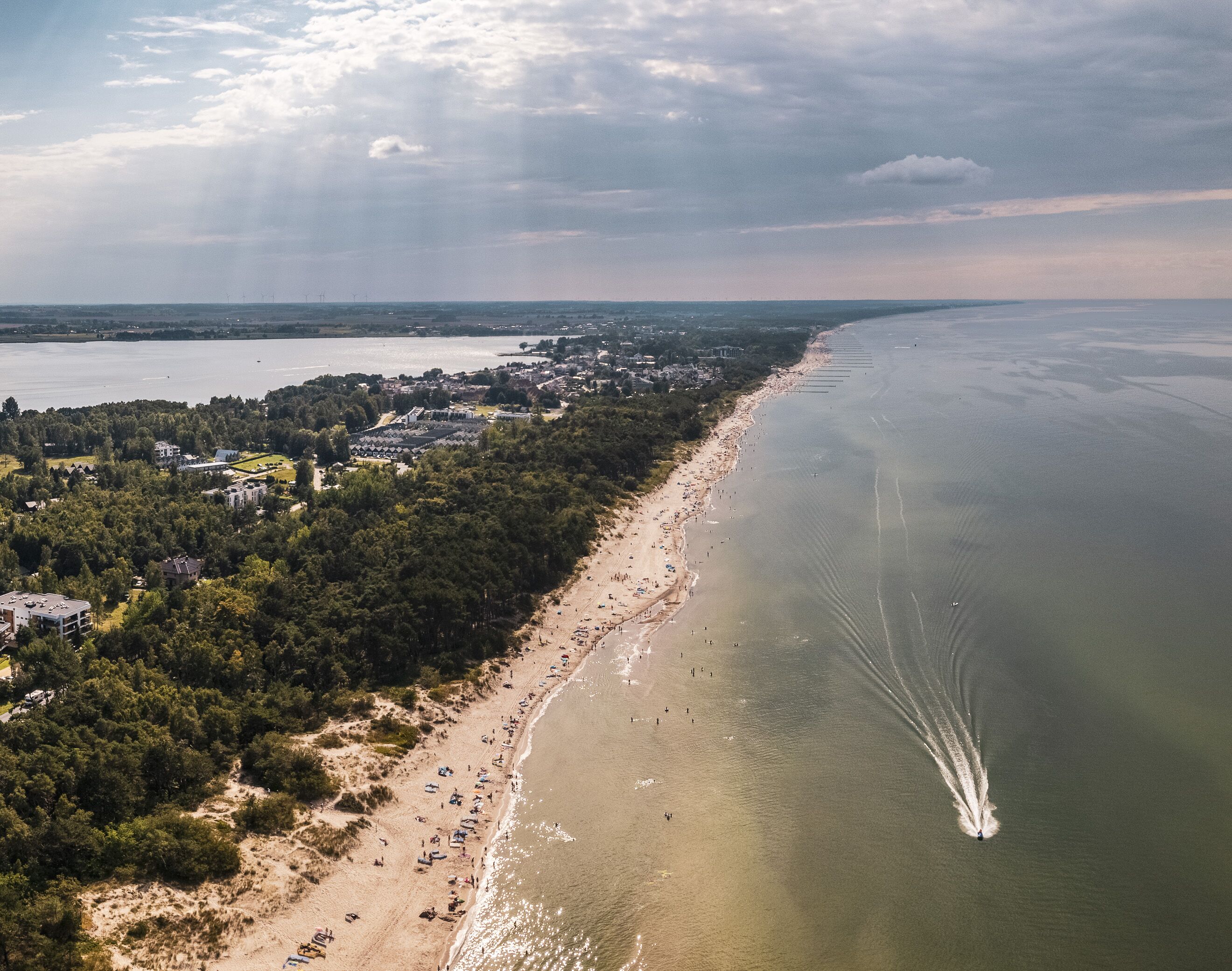 An aerial view of a coastal area with a beach, buildings, and a forested area.