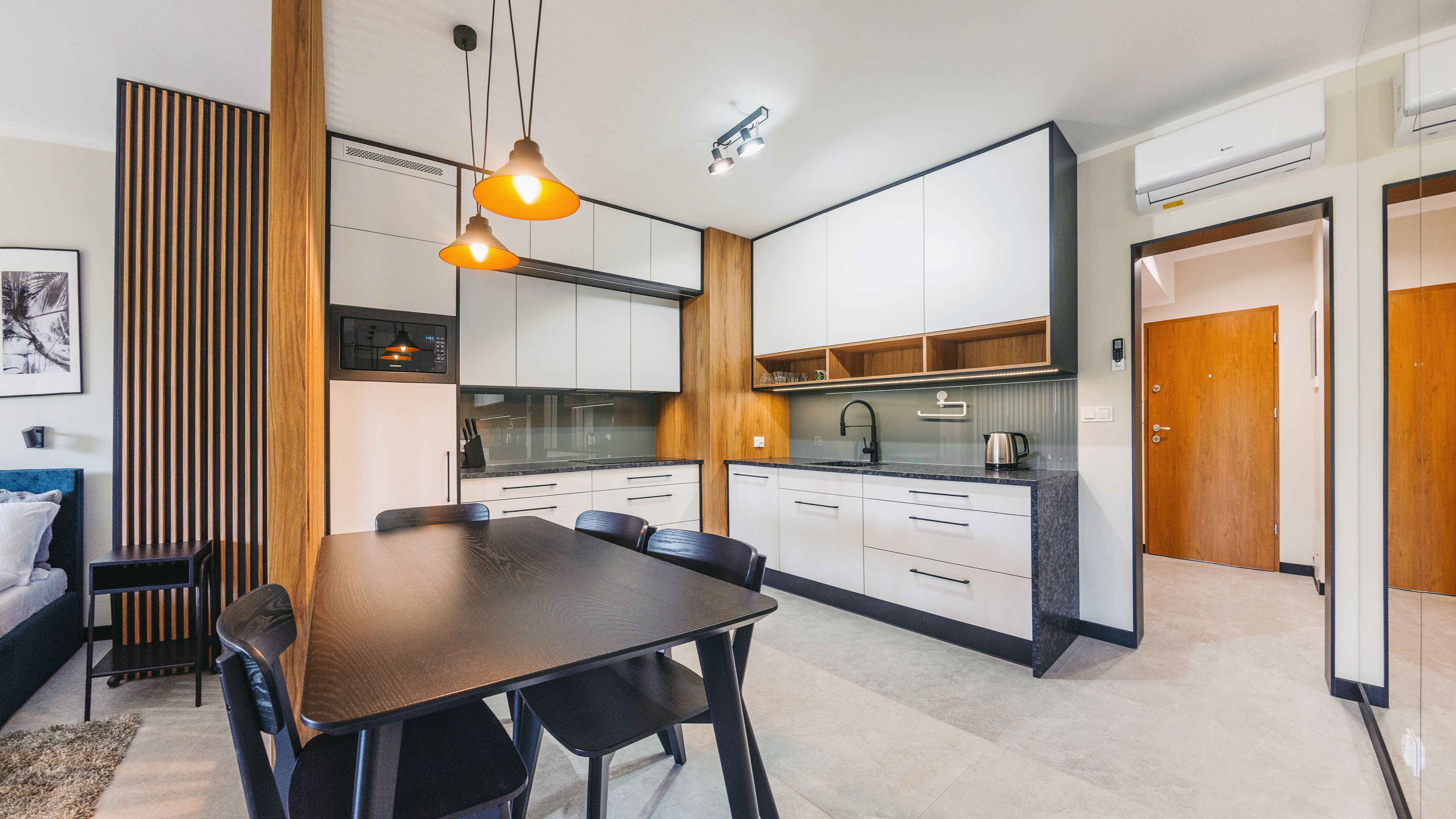 A modern kitchen with white cabinets, a wooden accent wall, and a dining area with a dark wooden table and chairs.