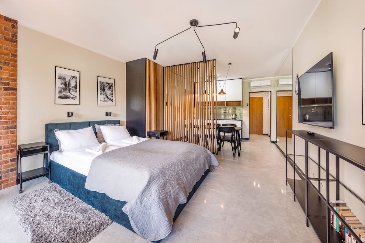 Een moderne hotelkamer met een groot bed, een bureau, een televisie en uitzicht op de keuken en de woonkamer.