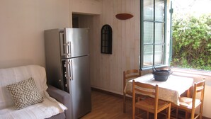 Eine kleine Küche mit Kühlschrank, einem Esstisch mit Stühlen, einem Fenster mit Jalousien und einer Holzwand.