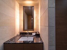 Un baño moderno con lavamanos de mármol, muebles de madera y un espejo grande.