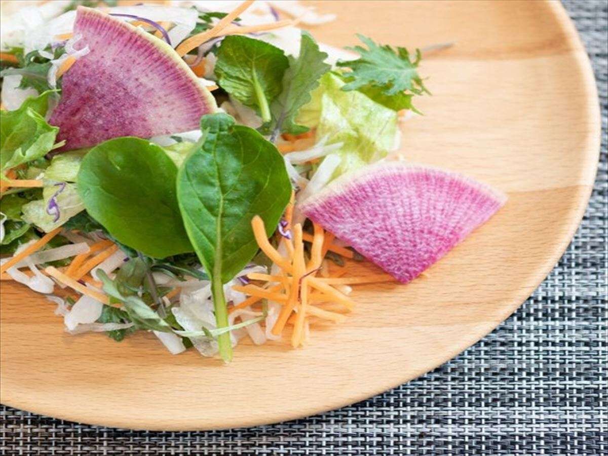 A wooden plate with a salad containing lettuce, shredded carrots, and purple leaves.