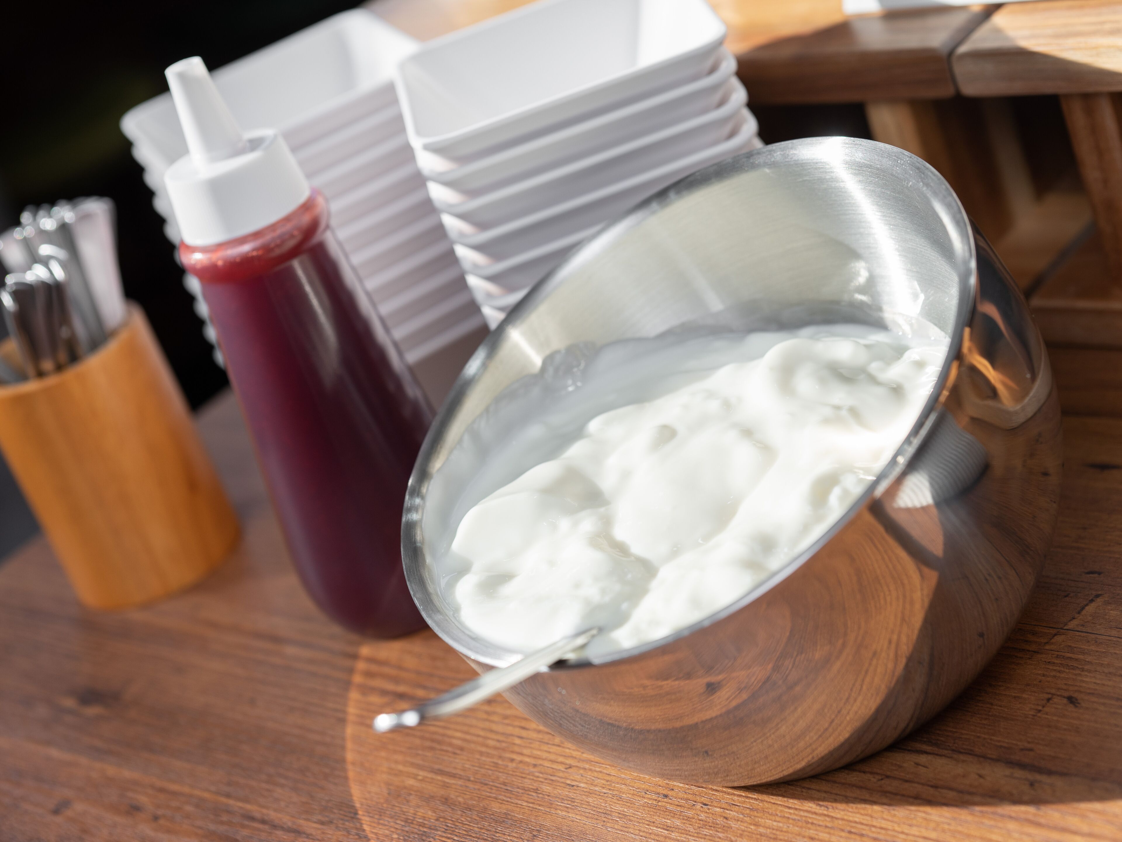 Un bol en métal contenant une substance blanche, une bouteille rouge et des assiettes blanches empilées sur une surface en bois.