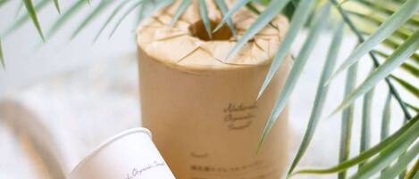 A brown paper container labeled "Natural, Organic, Small" and a white container with the same label, both placed on a surface with a palm leaf in the background.