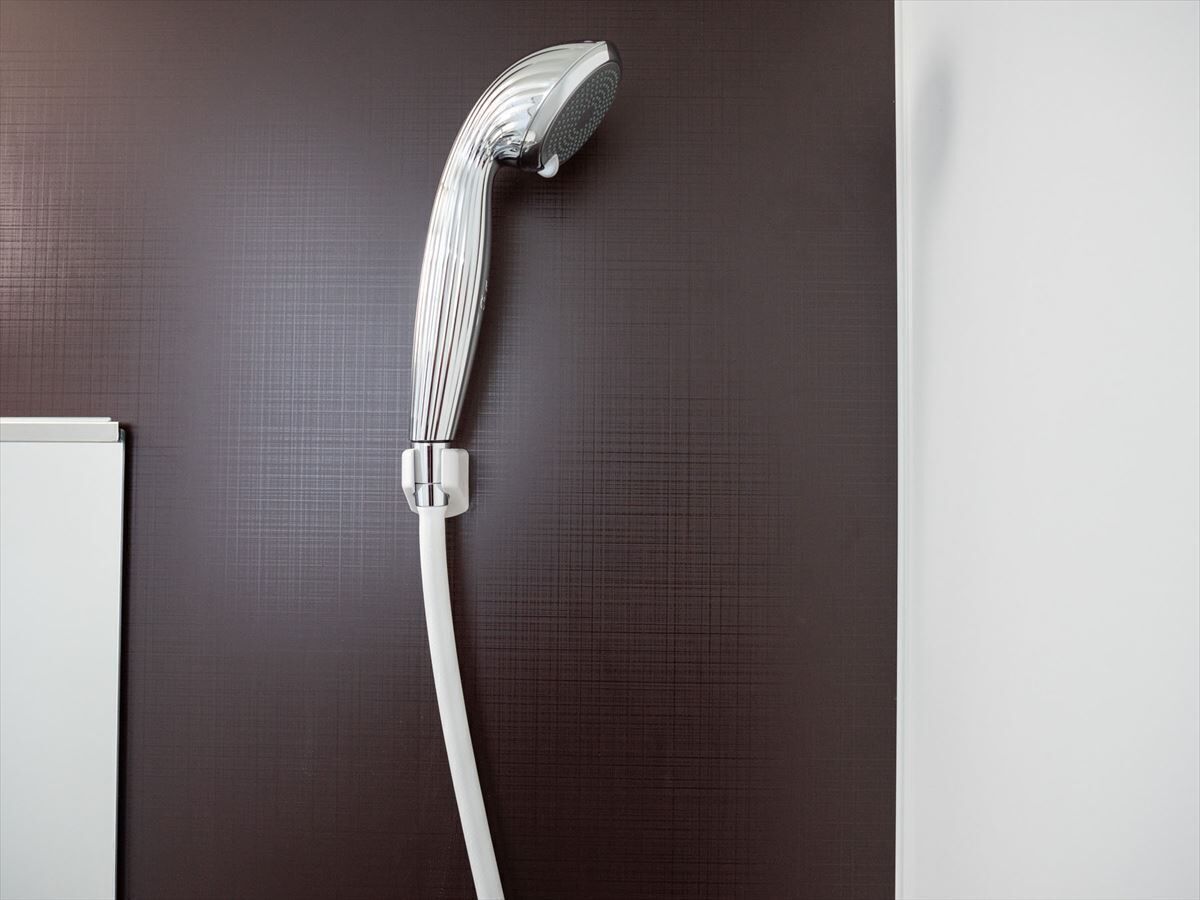 A modern showerhead with a curved design, mounted on a dark textured wall.