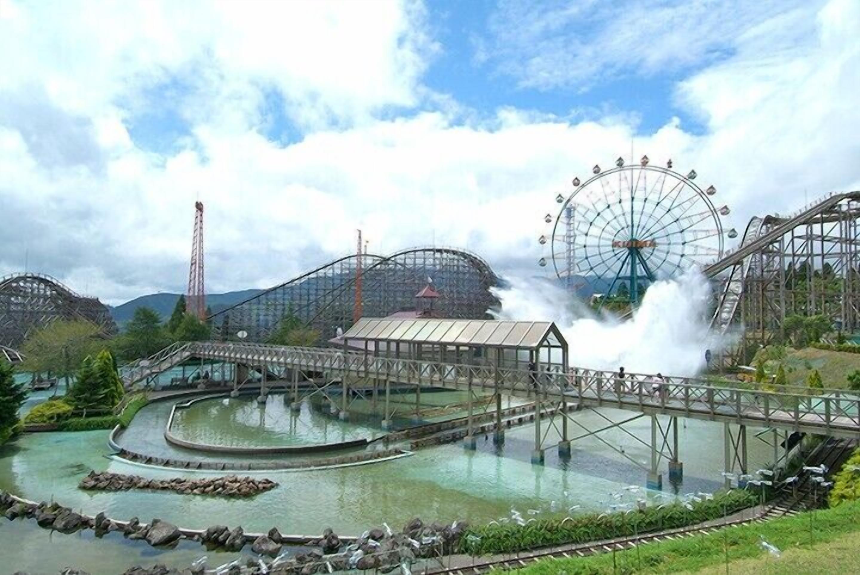 Des montagnes russes, une grande roue et un pont enjambant une étendue d’eau.