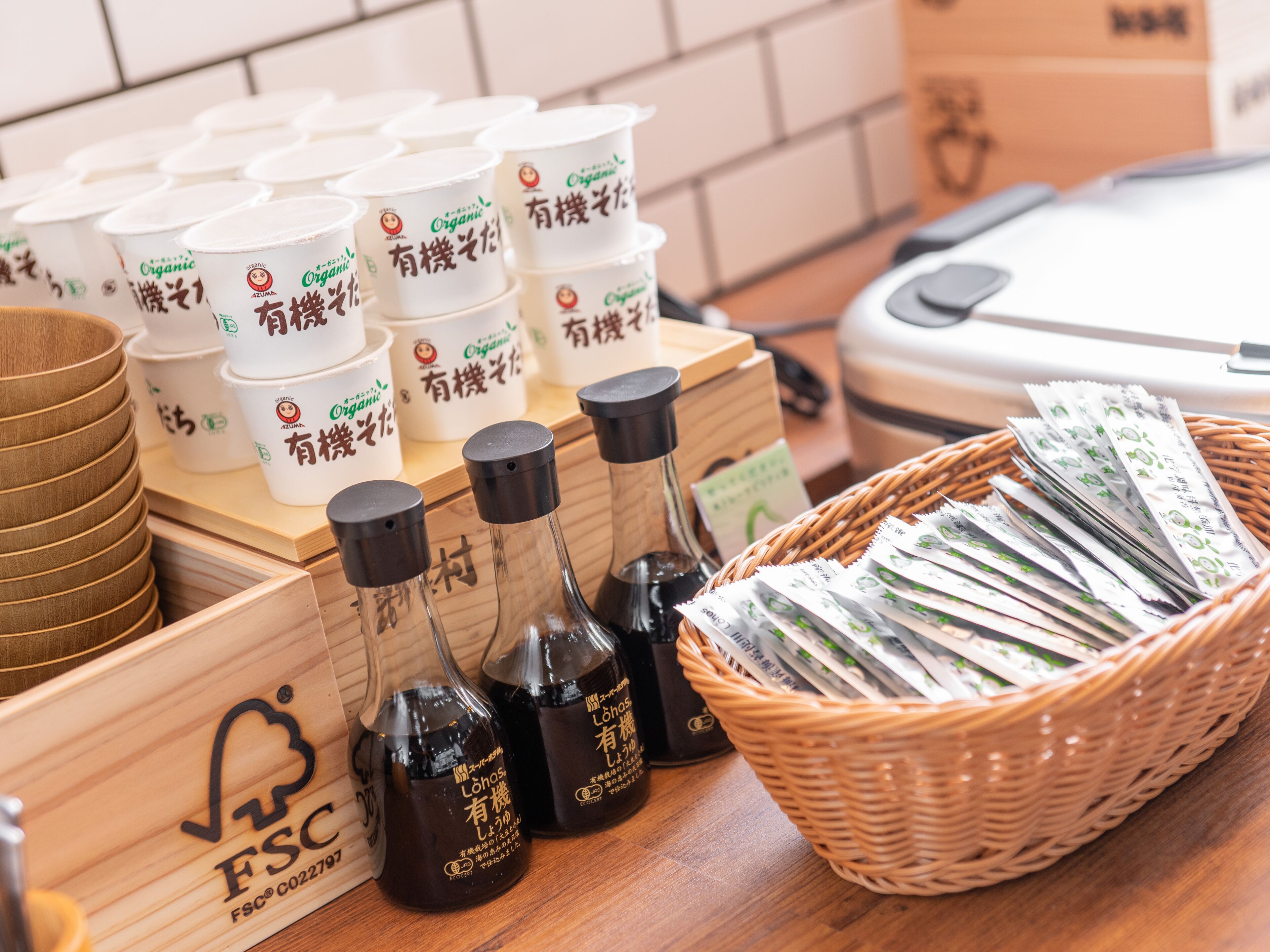 A table with various containers, including white cups with Japanese text, black bottles with labels, and a wicker basket filled with packets.