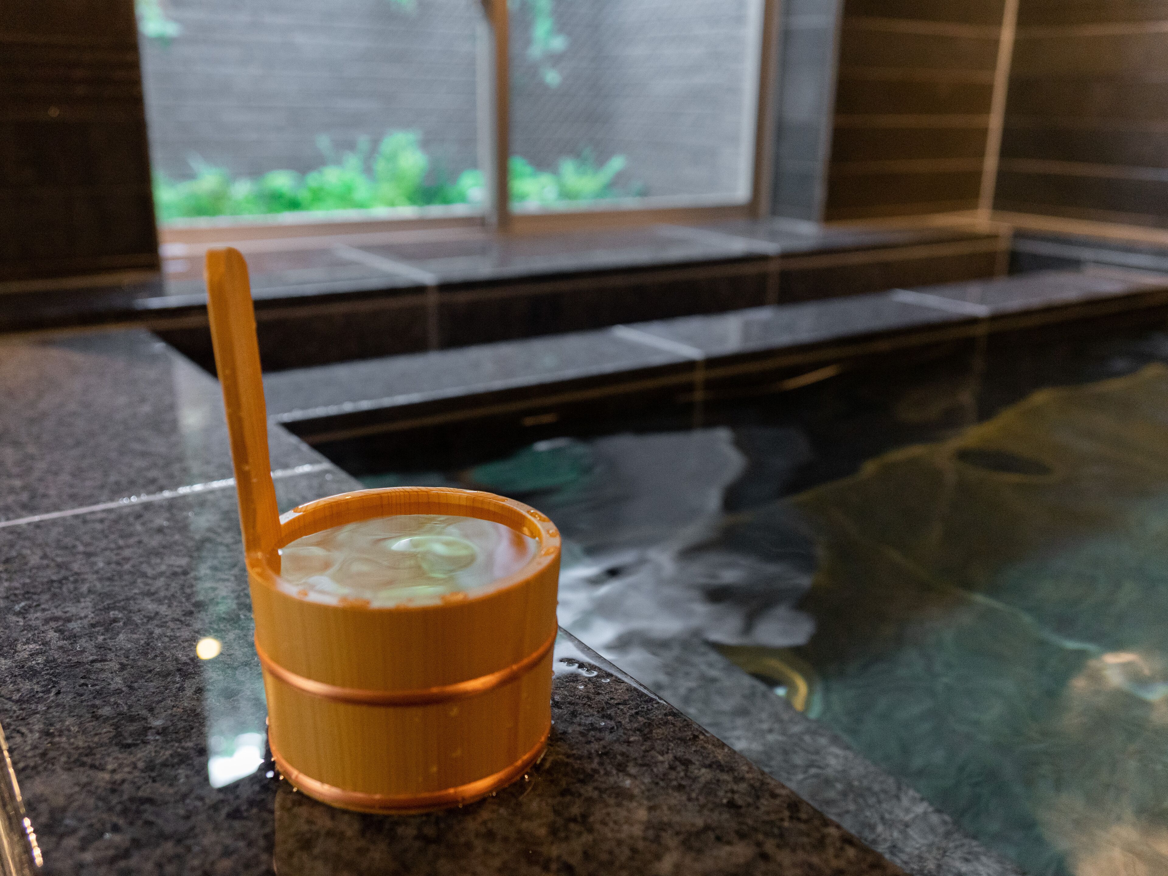 A small wooden bowl with a spoon on a granite countertop near a pool.