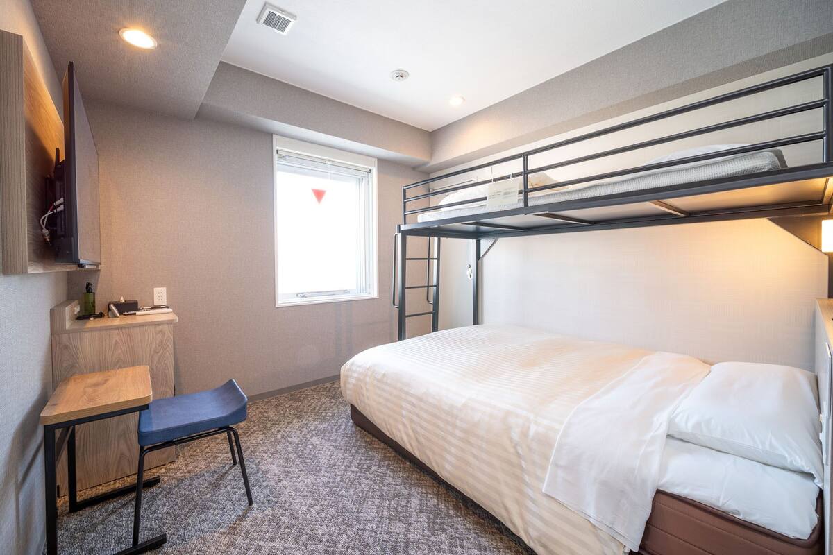 A bunk bed room with a desk, chair, and a window with blinds.