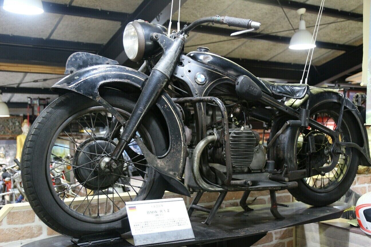 A vintage BMW R12 motorcycle displayed indoors, with a sign indicating its model and year.