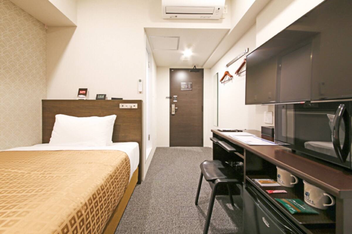 Quarto de hotel com cama, escrivaninha, cadeira, micro-ondas e ar condicionado.