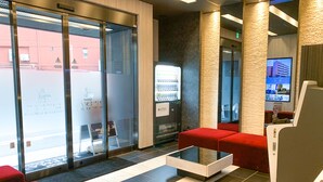 A lobby with a reception desk, red seating, a vending machine, and a television screen. - Hotel Livemax Chiba Chuo Ekimae (Chiba)