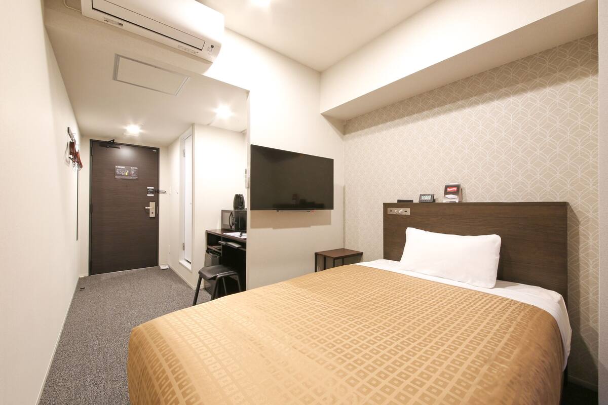 Quarto de hotel com cama, escrivaninha, televisão e aparelho de ar condicionado.