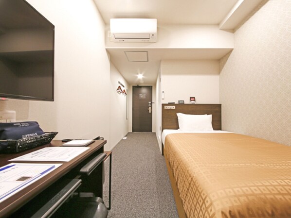 Une chambre d’hôtel équipée d’un lit, d’un bureau avec un ordinateur, d’une chaise, d’une télévision et d’un appareil de climatisation.
