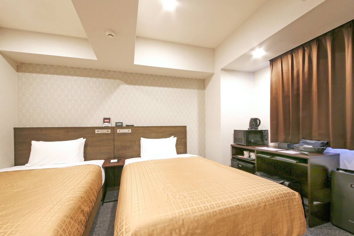 Quarto de hotel com duas camas, uma escrivaninha, um micro-ondas e uma cafeteira.