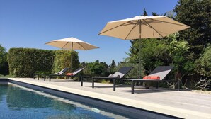 Zona junto a la piscina con sillones de descanso y sombrillas.