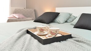 A neatly made bed with a grey blanket, a tray with two teacups and saucers, and a book on the bed.