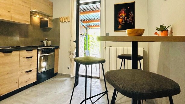 A modern kitchen with wooden cabinets, a stove, and a dining area with stools and a table.